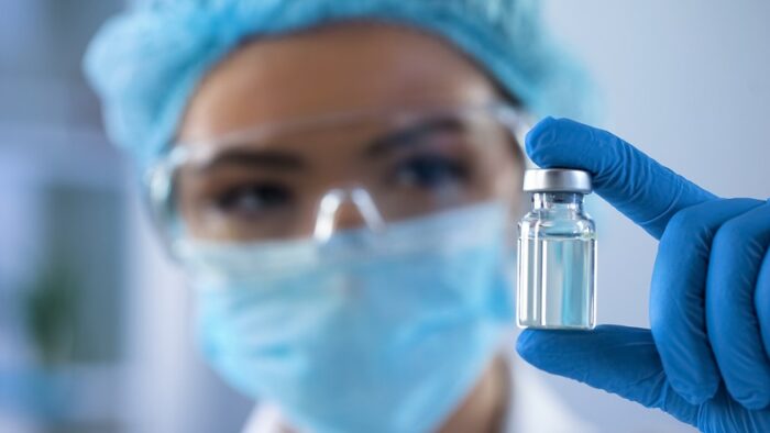 Vrouwelijke bioloog, die een fles met vaccine in een lab vasthoudt